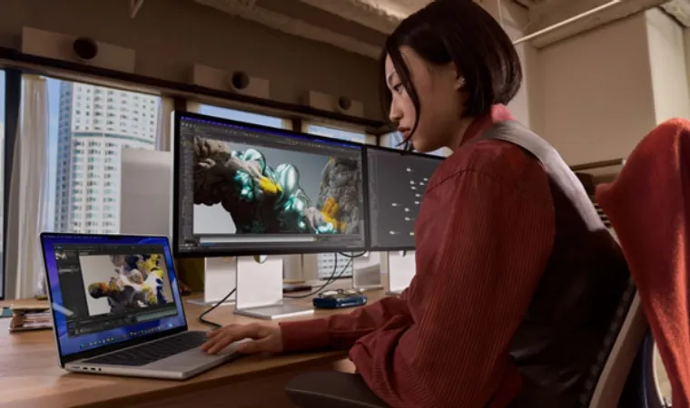 Foto de uma mulher usando um MacBook Pro M5 conectado a dois monitores externos enquanto edita imagens