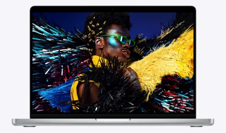 Foto de um MacBook Pro M5 aberto de frente exibindo a foto de um homem fantasiado com tiras de vinil multicoloridas