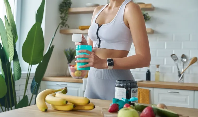 Mulher com roupas de academia está preparando uma vitamina com frutas e whey protein. 
