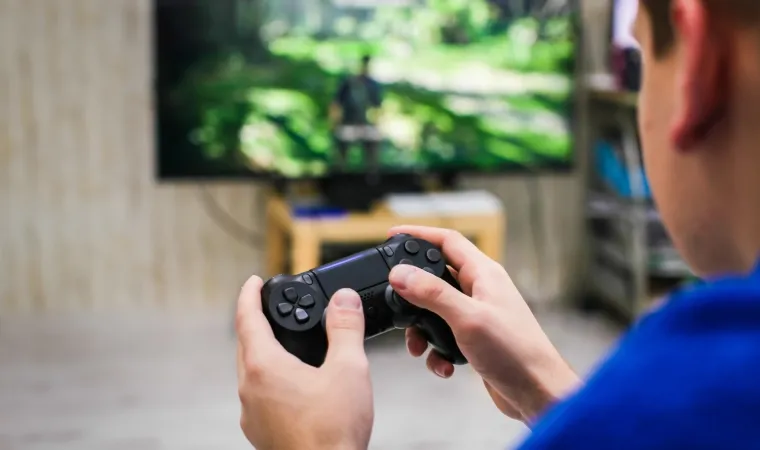 Jovem gamer joga com um Playstation ligado à TV em uma sala bem iluminada.