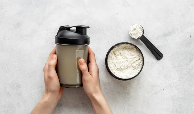 Garrafa shaker esportiva nas mãos e proteína whey no pote.