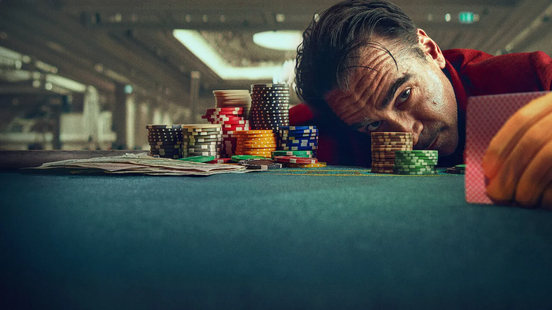 Imagem de homem debruçado sobre mesa de cassino cercada de fichas coloridas no filme Balada de Um Jogador