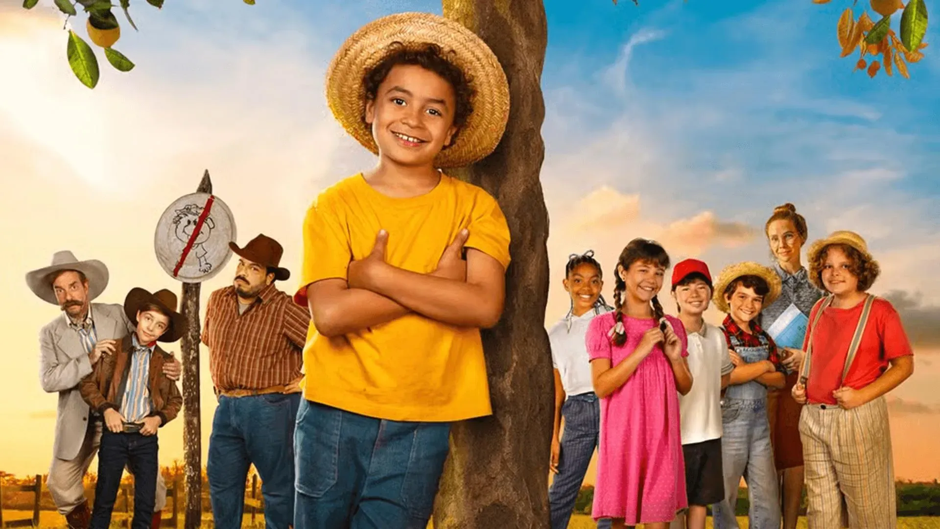 Menino com chapéu de palha e camiseta amarela encostado em uma árvore, cercado por outras crianças e adultos em cenário rural com céu azul