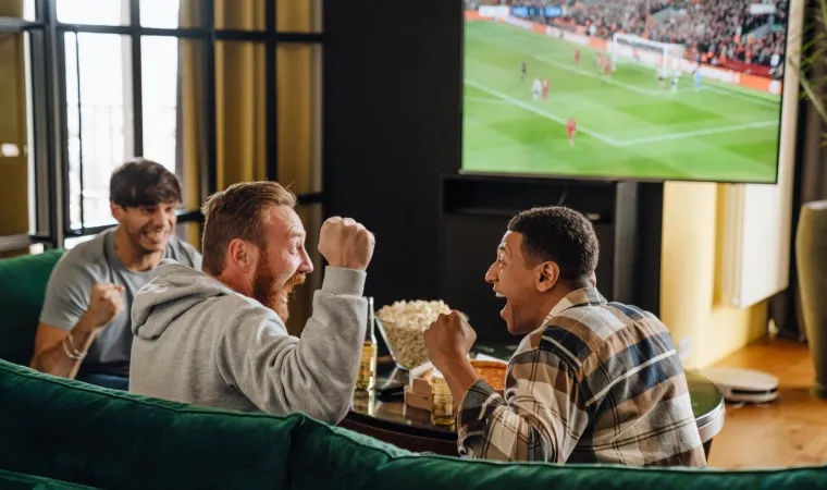 Grupo de amigos comemorando enquanto assistem futebol em uma TV