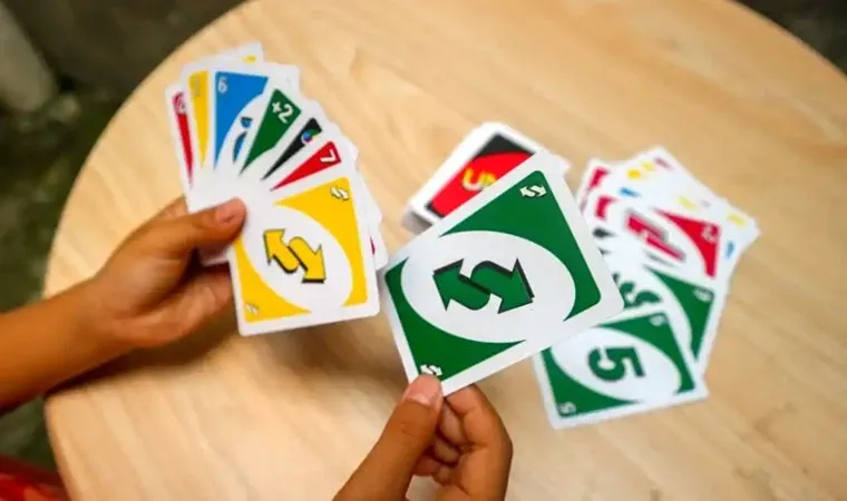 Jogador segurando sete cartas de UNO em sua mão esquerda e segurando uma carta Inverter verde na mão direita em frente a uma pilha de descarte 