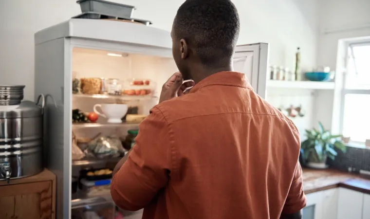Homem olhando geladeira aberta com alimentos dentro