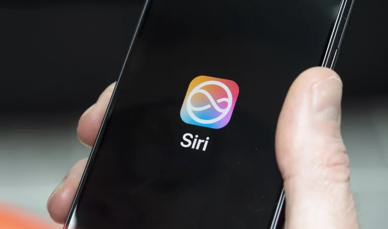 Imagem com zoom em uma mão segurando um celular com a logo da Siri na tela