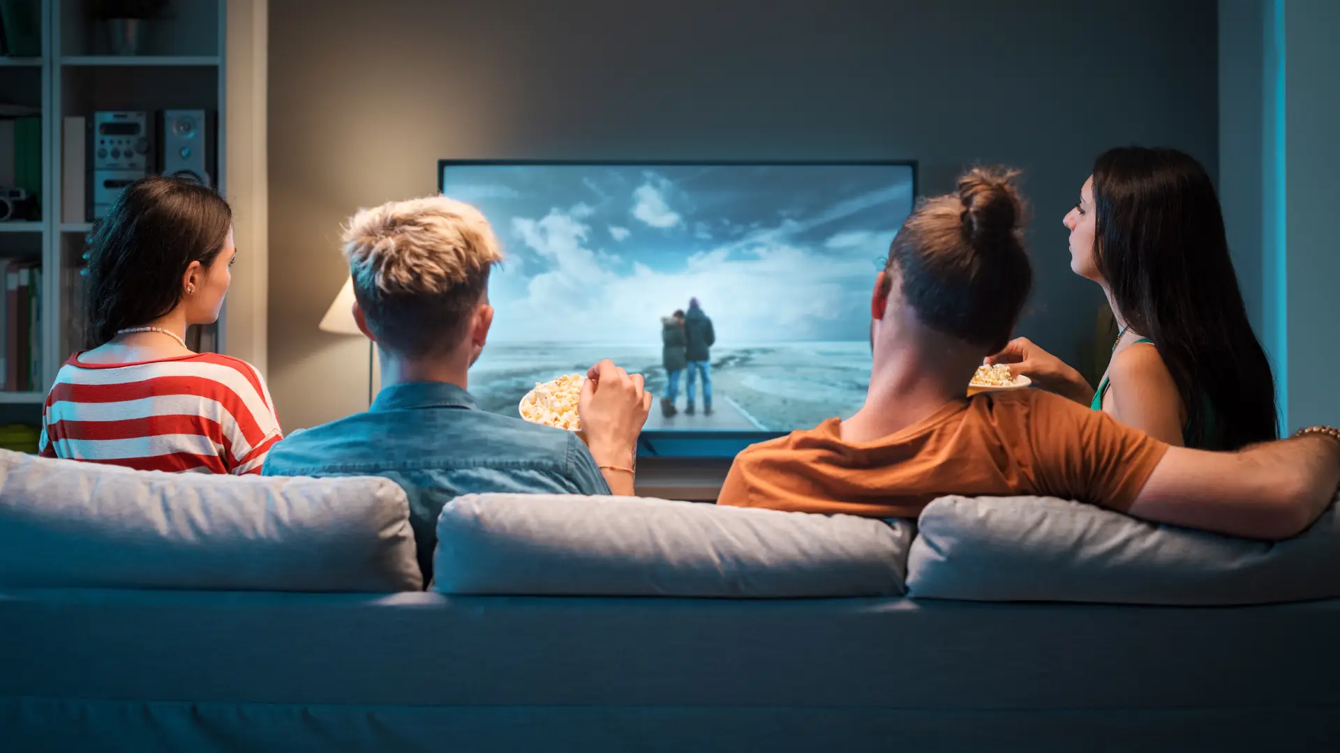 Imagem de quatro pessoas reunidas em um sofá assistindo um filme na TV.