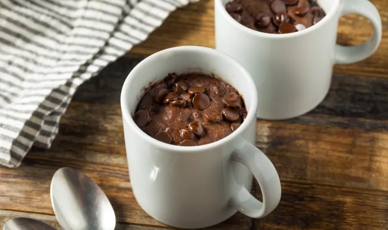 Duas xícaras brancas sobre mesa de madeira com bolo de caneca de chocolate