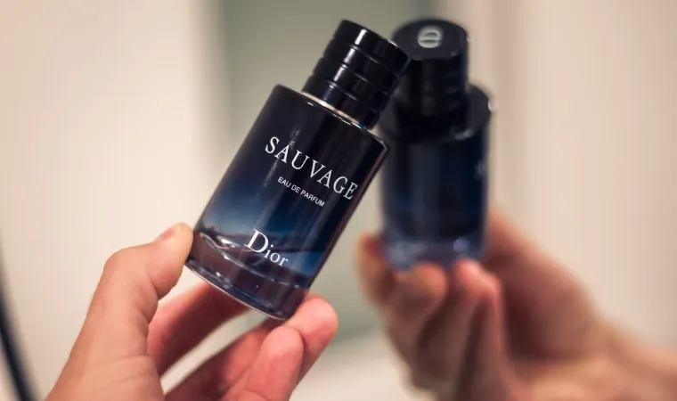mão segurando perfume Sauvage Dior em uma das mãos em frente ao espelho.