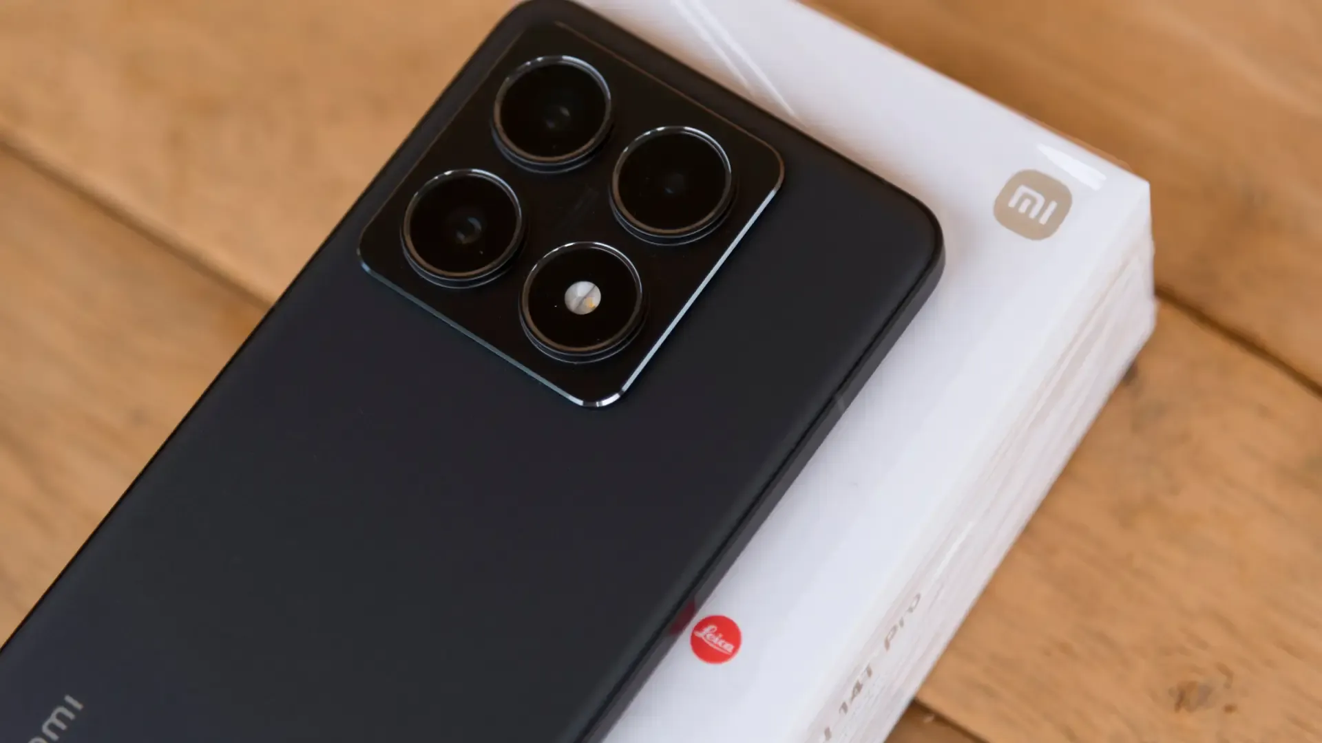 Imagem de celular Xiaomi na cor preta exibindo a parte traseira sob uma mesa de madeira